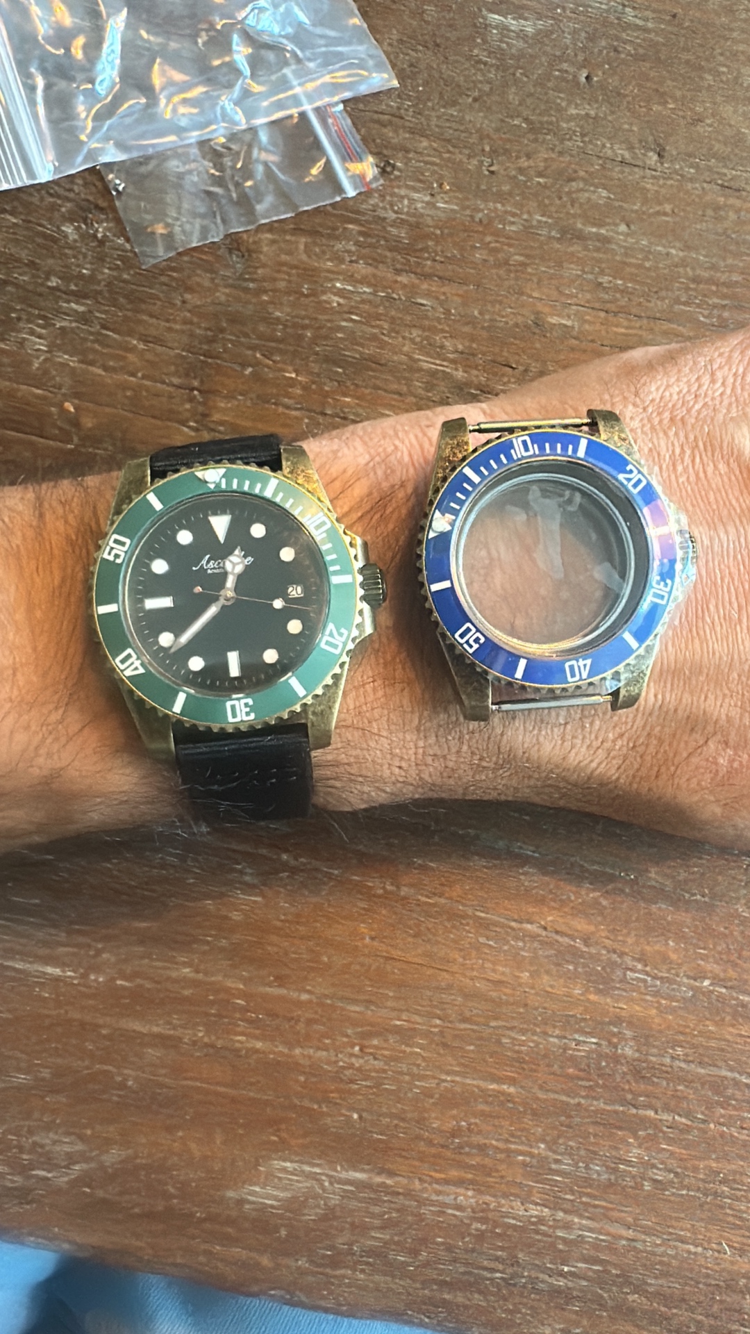 An early Ascanbe watch with a green bezel beside an empty blue-bezel case on the wrist